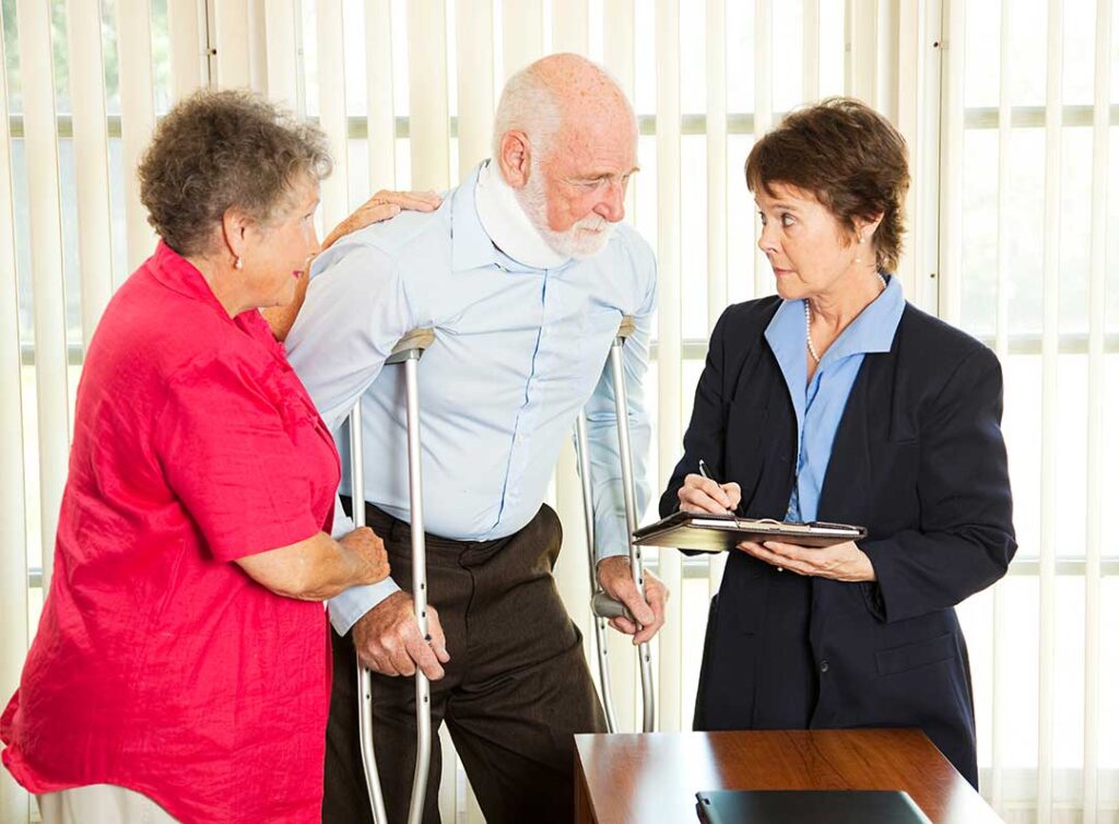 An insurance adjuster reviews paperwork and photographs at a desk with a laptop and medical bills visible.