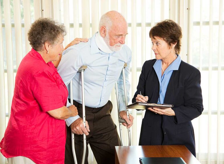 An insurance adjuster reviews paperwork and photographs at a desk with a laptop and medical bills visible.